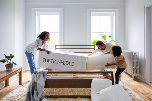 Family pulling a Tuft & Needle Mattress out of it's box and putting it on a bed frame