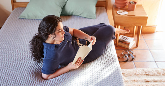 Woman reading a book laying on an unmade Tuft & Needle mattress