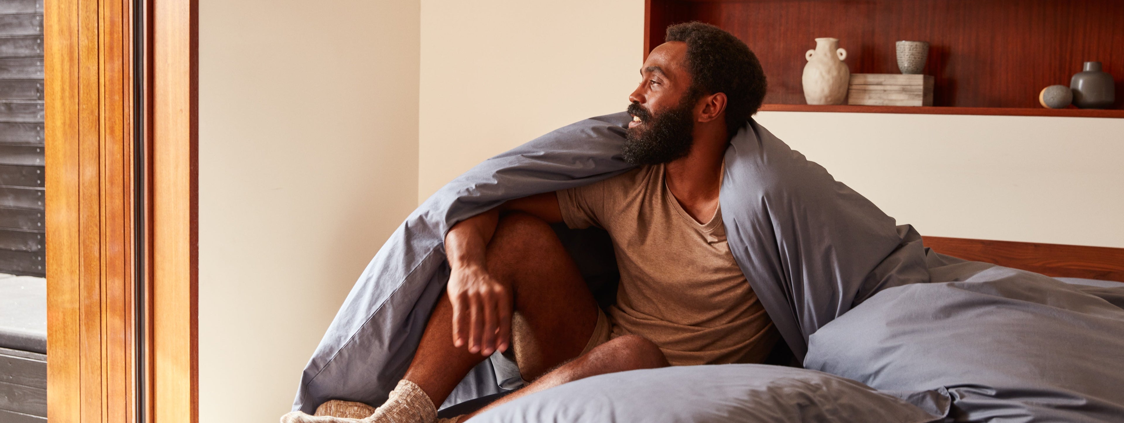 Man sits in bed covered in the percale duvet 