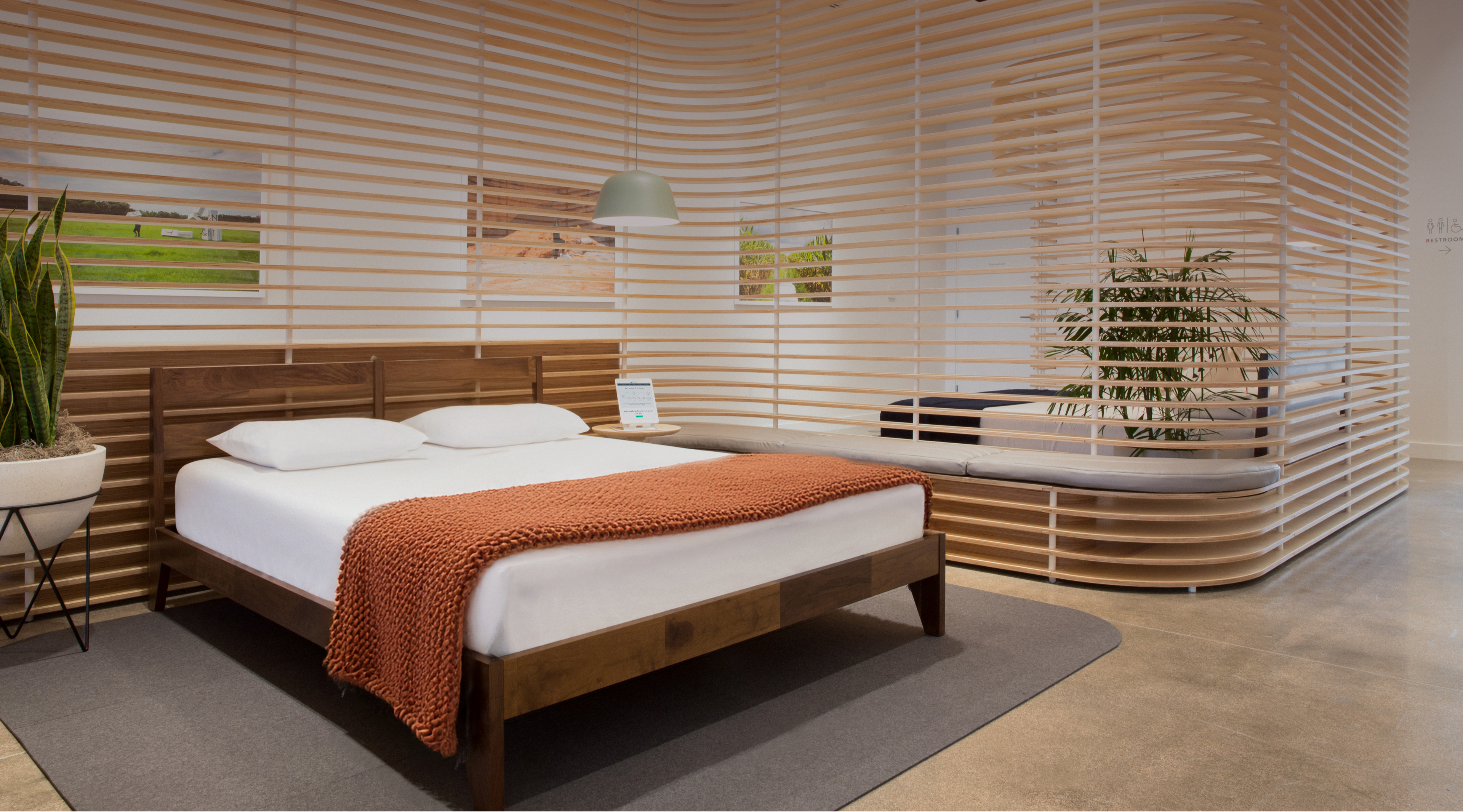 Tuft & Needle store with a wooden bed frame, mattress, blanket, and modern slatted wood room dividers.