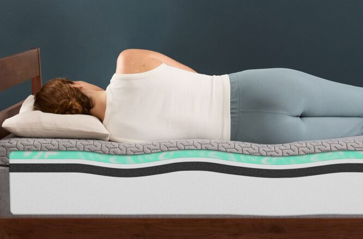 Person lying on their side on a Tuft & Needle all-foam mattress with visible internal foam layers in a cutaway view