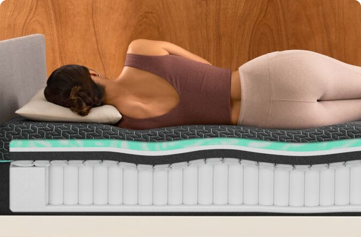 A woman lies on her side on a multi-layered mattress with a cross-section showing foam and coil layers.