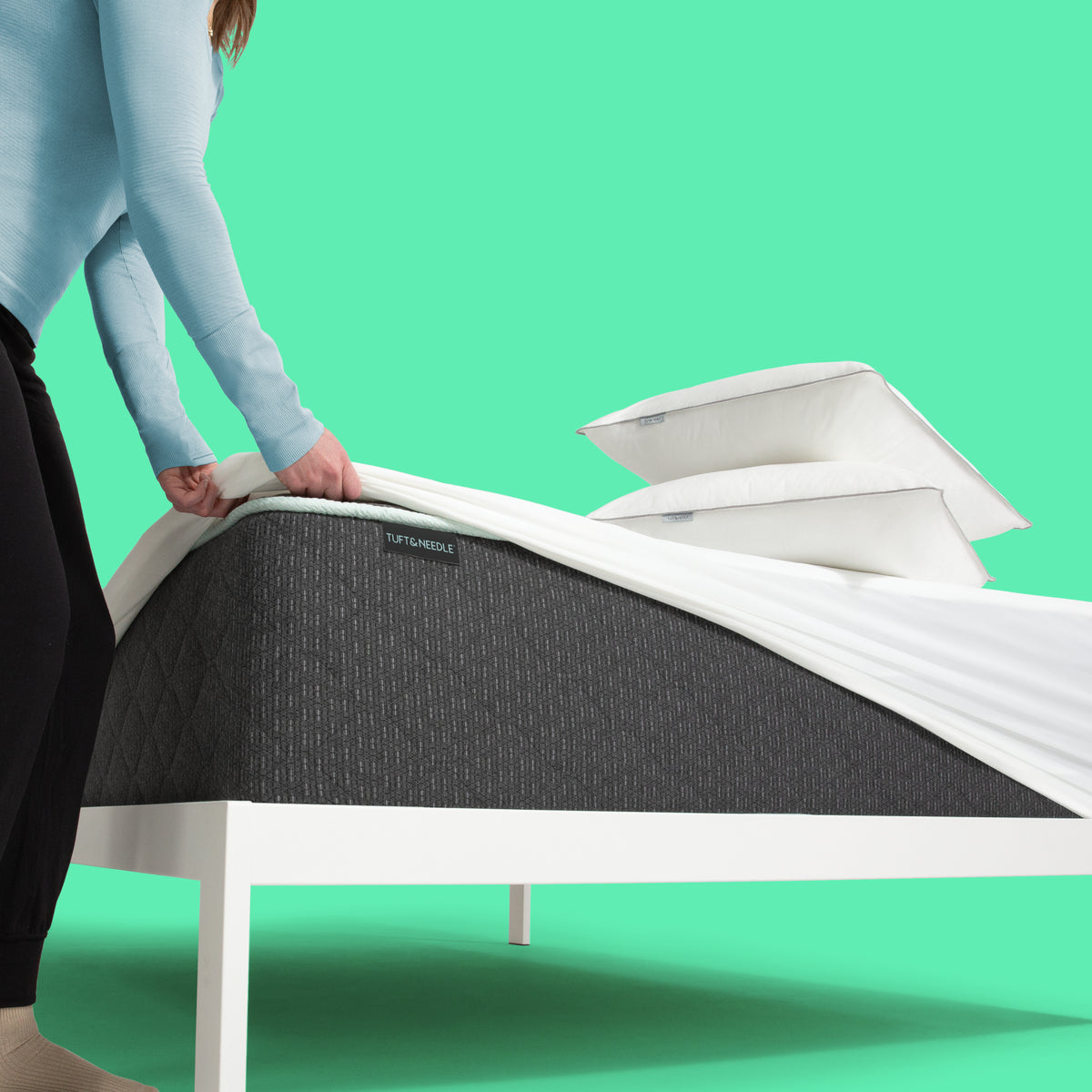 Person fitting a Tuft & Needle mattress protector over a Tuft & Needle Mint Luxe Plush Hybrid mattress
