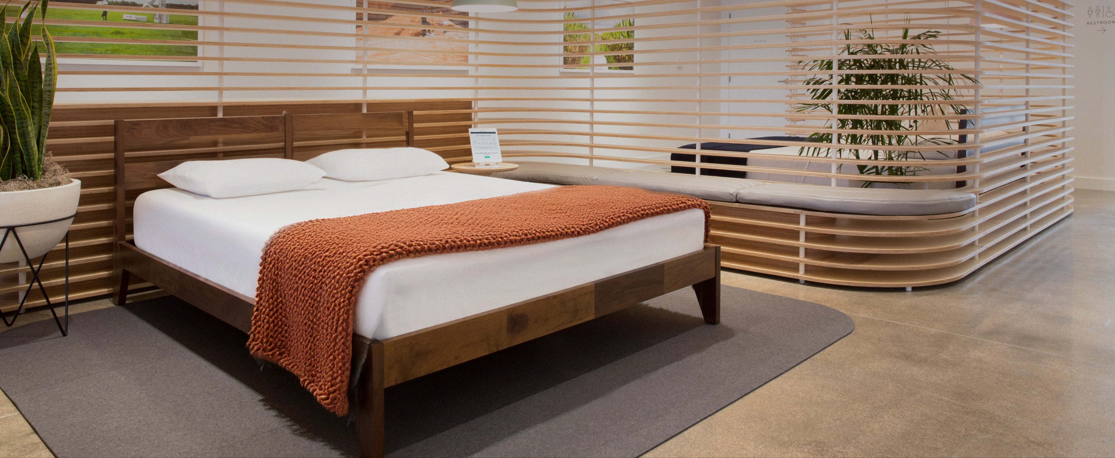 Tuft & Needle store with a wooden bed frame, mattress, blanket, and modern slatted wood room dividers.